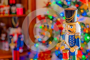 A nutcracker plays a drum in front of Christmas tree and armoire