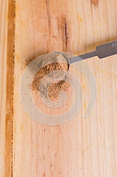 Nutmeg powder in measuring spoon close up with wooden neutral background