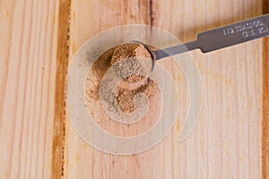 Nutmeg powder in measuring spoon close up with wooden neutral background