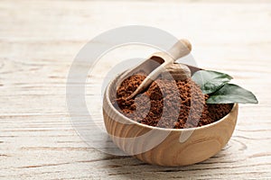 Nutmeg powder and seed with green leaves in bowl on white wooden table, space for text