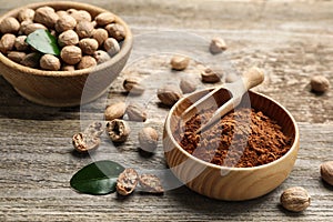 Nutmeg powder and seeds with green leaves on wooden table