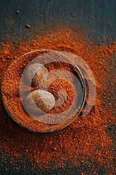Nutmeg whole and ground. Nutmeg fruits in nutmeg powder in a cup on a black slate background. View from above .Spices