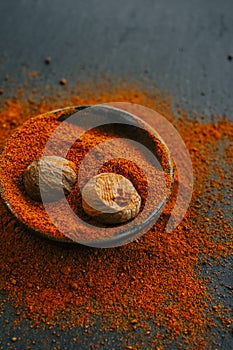 Nutmeg whole and ground. Nutmeg fruits in nutmeg powder in a round cup on a black slate background