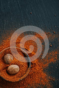 Nutmeg whole and ground. Nutmeg fruits in nutmeg powder in a round cup on a black slate background. View from above