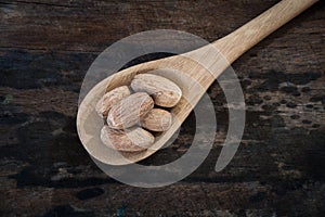 Nutmeg on wooden spoon over wooden background.