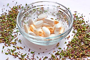 Nutritional supplements pills in a bowl on dried herbs background. Alternative herbal medicine, naturopathy and homeopathy