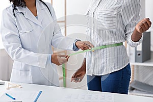 Nutritionist afro woman measuring patient`s waist in clinic