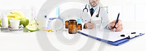 Nutritionist doctor writes the medical prescription for a correct diet on a desk with fruits, drugs and supplements, web banner