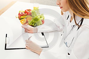 Nutritionist doctor writing diet plan on table