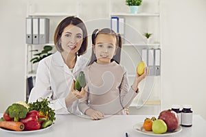 Nutritionist and little child at table with fresh vegetables, fruit and vitamins