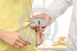 Nutritionist measuring patient`s body fat with digital caliper in clinic