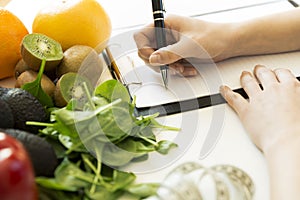 Nutritionist woman writing diet plan on table full of fruits and photo