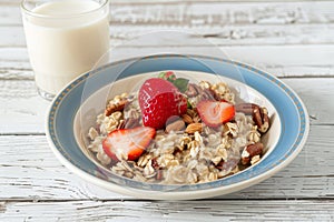 Nutritious breakfast oatmeal with strawberries and nuts, glass of milk on white wooden table