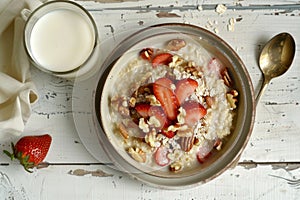 Nutritious breakfast, oatmeal with strawberries and nuts, milk in glass on wooden table, top view