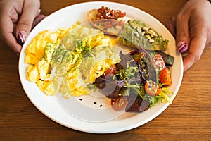 A nutritious brunch serving with fluffy scrambled eggs, a vibrant mixed salad, avocado toast, and seeds.