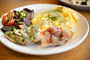 A nutritious brunch serving with fluffy scrambled eggs, a vibrant mixed salad, avocado toast, and seeds.