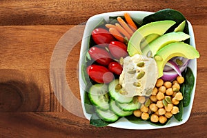 Nutritious lunch bowl with avocado, hummus and vegetables on wood