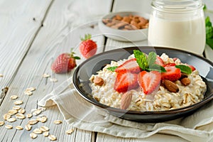 Nutritious oatmeal bowl with fresh strawberries, nuts and milk on white wooden table