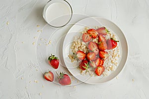 Nutritious oatmeal and strawberries on white plate with milk, set on elegant white table top view