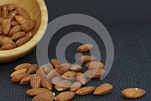 Nuts almonds poured out of a bamboo bowl, on a dark background, healthy diet for weight loss