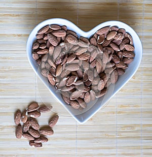 Nuts arranged in heart  on background. Healthy Food image close up almond on the cup plate. Love Texture on top view mock up