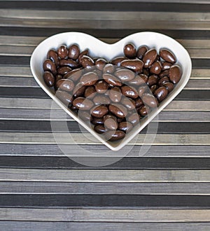 Nuts arranged in heart shape on background. Food image close up candy, chocolate milk, extra dark almond nuts. Love Texture