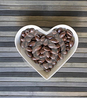 Nuts arranged in heart shape on background. Food image close up candy, chocolate milk, extra dark almond nuts. Love Texture
