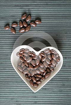 Nuts arranged in heart shape on background. Food image close up candy, chocolate milk, extra dark almond nuts. Love Texture