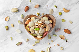 Nuts mixed in heart wooden bowl on marble table