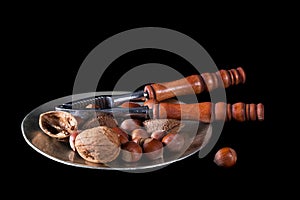 Nuts with nutcrackers on plate, black background.