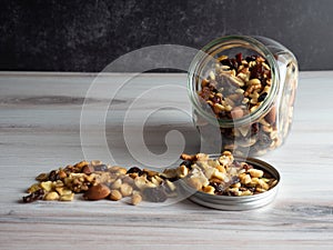 Nuts, seeds and dried fruits spilling out of a clear glass jar into the lid and onto the table!  Healthy, nutrient packed good