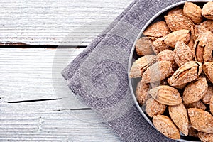 nuts snack almond on metal plate on dark grey linen napkin on white wooden background, top view on right side