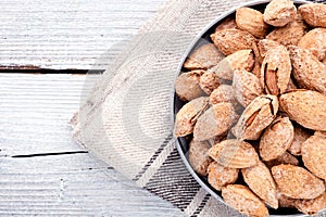 nuts snack almond on metal plate on light grey linen napkin on white wooden background, top view on right side