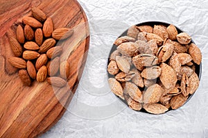 nuts snack salted almonds in shell in metal plate and on wooden board on white baking paper top view