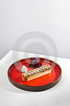 Nuts tartlet with blackberry ice cream on red ceramic dishware. Caramel and hazelnut tart in minimalistic style. Modern dessert on