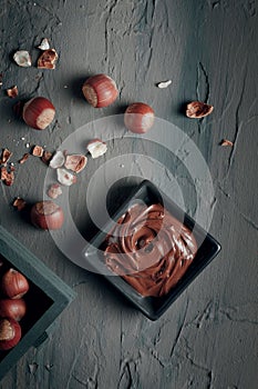 Nutty chocolate paste in a square dish on a dark gray slate, stone or concrete table. Top view. There are a lot of