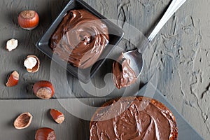 Nutty chocolate paste in a square dish on a dark gray slate, stone or concrete table. Top view. There are a lot of