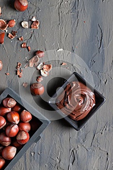 Nutty chocolate paste in a square dish on a dark gray slate, stone or concrete table. Top view. There are a lot of