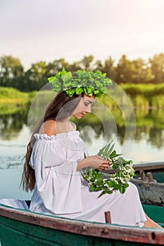 The nymph with long dark hair in a white vintage dress sitting in a boat in the middle of the river.