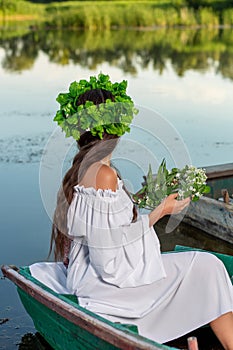 The nymph with long dark hair in a white vintage dress sitting in a boat in the middle of the river.