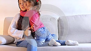 NYoung mother sitting on couch and gives small daughter phonen