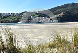 Small fishing village from beach with grass on sand dunes. O Barqueiro or El Barquero, Galicia, Spain.