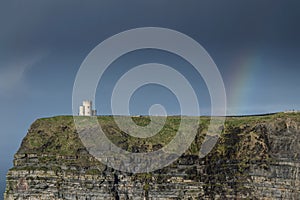 O`Brien`s Tower and colorful rainbow in blue sky. Cliff of Moher, Ireland. Famous travel destination. Irish luck concept