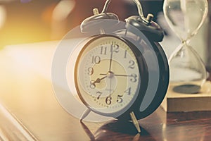 8 o`clock time retro clock with sand hourglass on wood table with sun light background