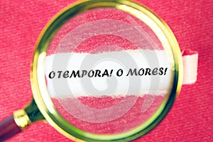 o tempora, o mores (O, the times O, the morals) Latin phrase through a magnifying glass under a torn piece of paper