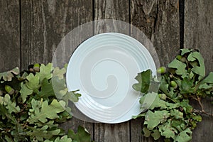 Oak leaves and clean white empty plate on old wooden table