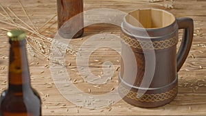 Oak mug with a handle and a glass brown bottles on a wooden table in a pub or bar. Brown mug with ornament, wheat grains