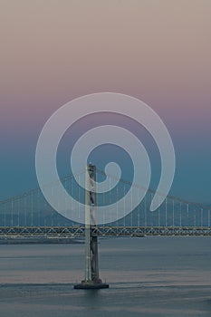 The Oakland Bay Bridge on the water under a pink and blue sky in San Francisco, California