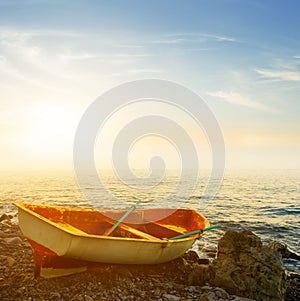 Oared boat on stony sea coast at the sunset