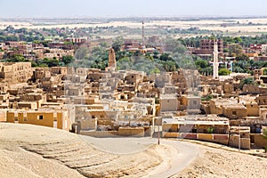 Oasis with ruins. Ancient middle eastern Arab town built of mud bricks, old mosque, minaret. New city in back. Al Qasr, Dakhla,